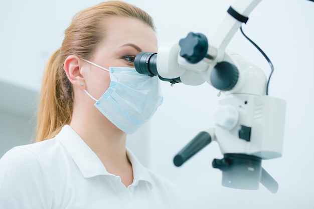 Portrait of a dentist wearing a medial mask and looking through the microscope ocular