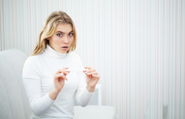 Portrait of desperate young woman holding pregnancy test stick