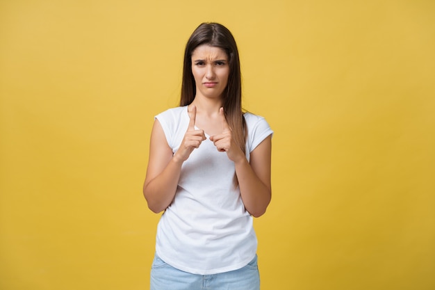 Portrait disappointed awkward attractive woman in white shirt, raising hand and shaping small item, looking at fingers and frowning from dislike and regret, standing over yellow background.