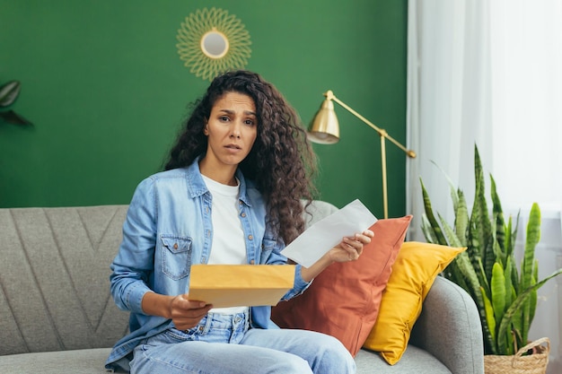 Portrait of disappointed and sad woman hispanic woman with received envelope looking frowning at