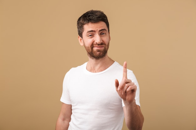 Portrait of a disappointed young man casually dressed showing stop gesture isolated over beige