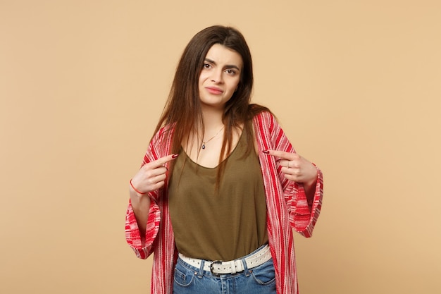 Portrait of dissatisfied young woman in casual clothes pointing index fingers on herself isolated on pastel beige background in studio. People sincere emotions, lifestyle concept. Mock up copy space.