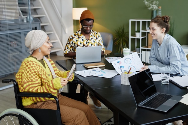 Portrait of diverse creative team working in office with focus on young woman using wheelchair at bu