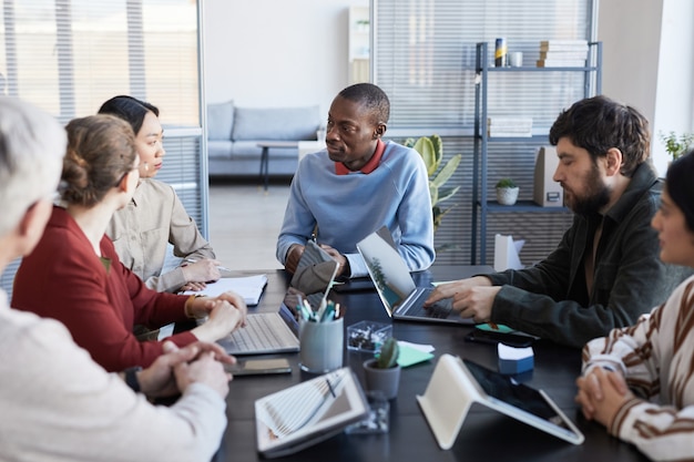 Portrait of diverse group of business people at table collaborating during briefing meeting in office, focus on smiling African-American man