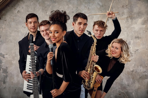 Portrait of diverse group of young people musical band playing with instruments on gray concrete background