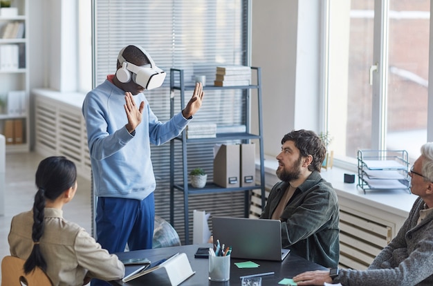 Портрет разнородной ИТ-команды, разрабатывающей программное обеспечение для проекта виртуальной реальности, фокусируется на афроамериканском мужчине с гарнитурой VR в офисе