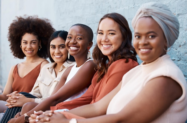 Foto diversità di ritratti e un gruppo di donne d'affari felici sedute in fila come colleghe contro un muro fuori città