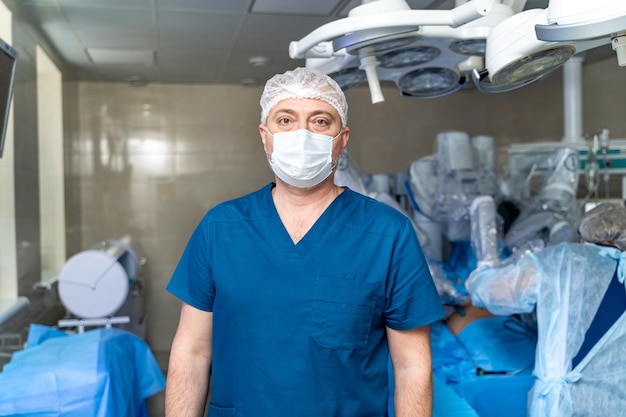 Portrait of doctor in glasses standing in operating room Professional surgeon in blue uniform and protective face mask