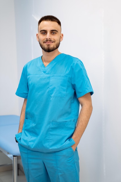 Portrait of a doctor or medical specialist. Modern office background. Man in scrubs stands with hands in pockets.