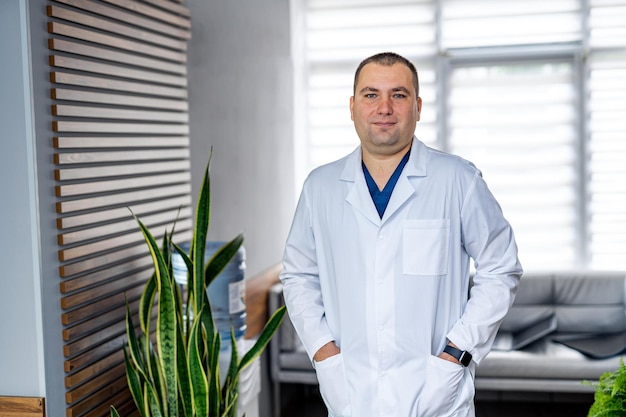 Foto ritratto di un medico o di un medico specialista. ritratto verticale. uomo in camice seduto a tavola con le mani in tasca.