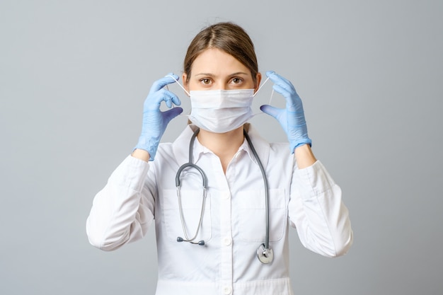 Portrait of doctor putting sterile mask isolated on gray