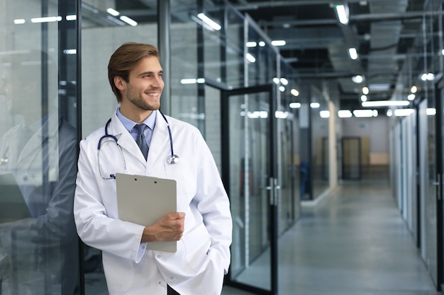 Portrait of doctor standing in hospital corridor wearing lab coat and stethoscope.