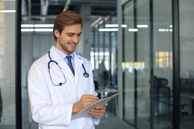 Portrait of doctor standing in hospital corridor wearing lab coat and stethoscope.