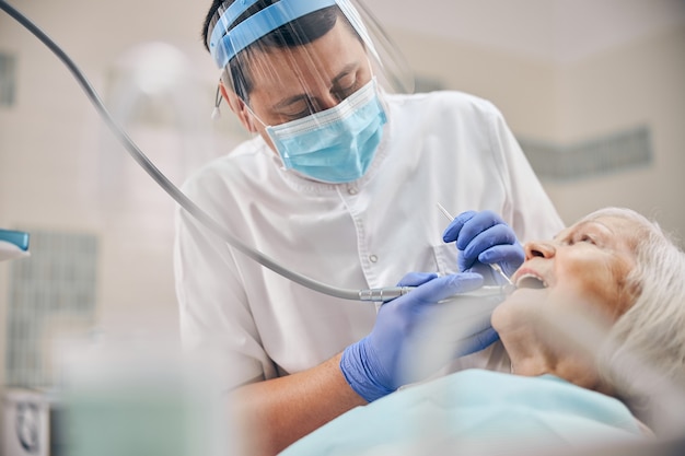 Портрет врача, лечящего женские зубы стоматологическими инструментами и зеркало с угольной дрелью в стоматологической клинике