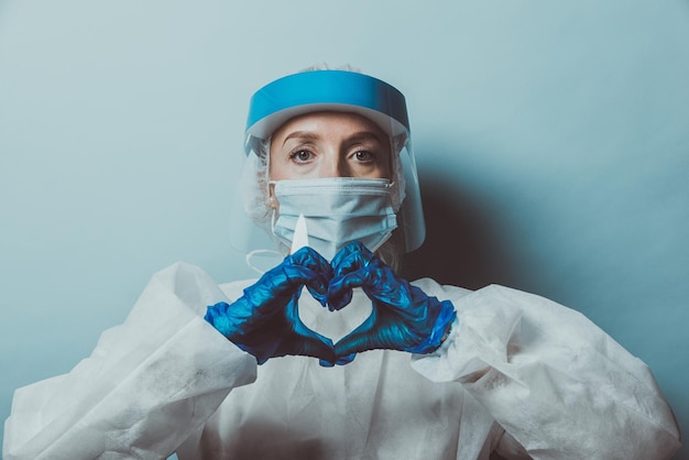 Photo portrait of doctor wearing mask making heart shape against wall