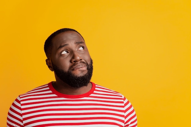 Portrait of doubrful nervous man look up empty space think bite lip on yellow background