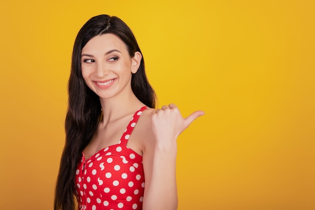 Portrait of dreamy adviser woman direct thumb side look empty space wear dotted red dress on yellow background