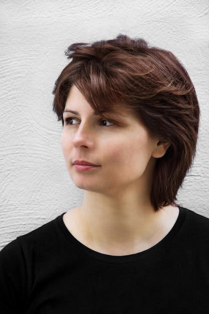 Portrait of dreamy beautiful young woman with brown hair on white wall