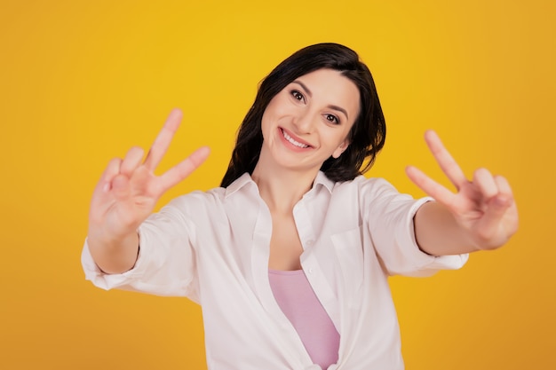 Portrait of dreamy funny positive girl show two v-signs on yellow background