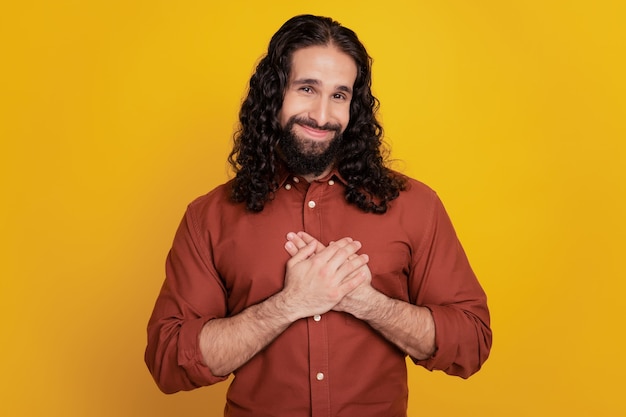 Portrait of dreamy grateful guy hands chest look camera on yellow background