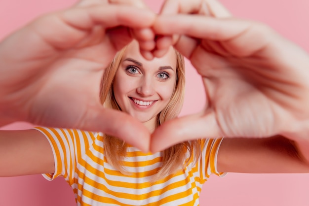 Portrait of dreamy romantic girl heart gesture cover face on pink background