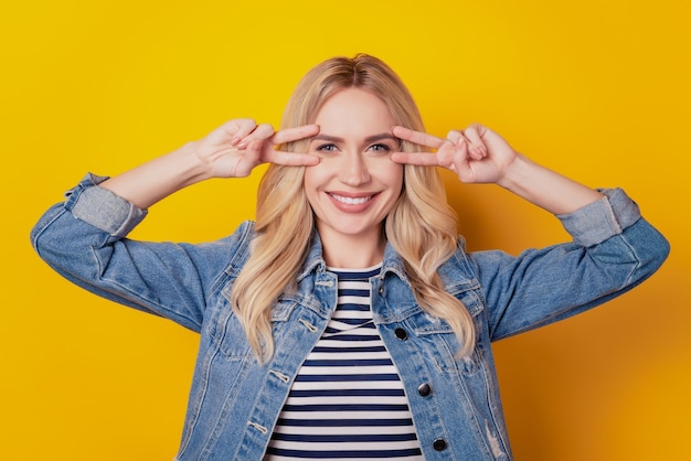 Ritratto di una donna splendida e sognante che mostra una telecamera con lo sguardo della copertina del v-sign in posa su sfondo giallo