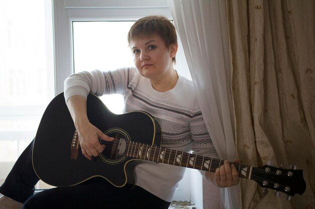 Portrait of dreamy woman with guitar near window at home, close up