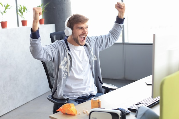 Portrait of ecstatic gamer guy in headphones screaming and rejoicing while playing video games on computer.