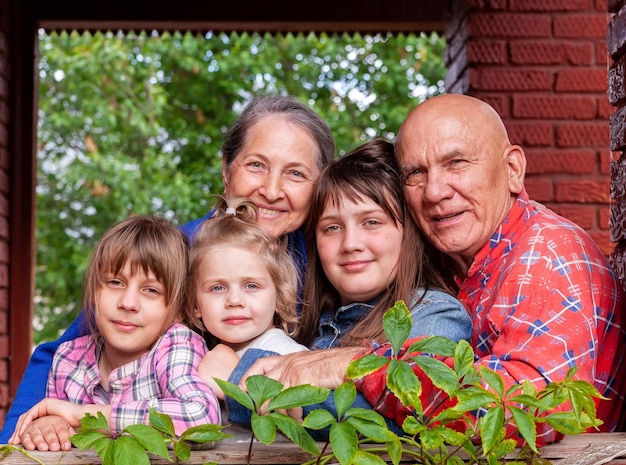 Портрет пожилых бабушек и дедушек с тремя внучками на крыльце деревенского дома
