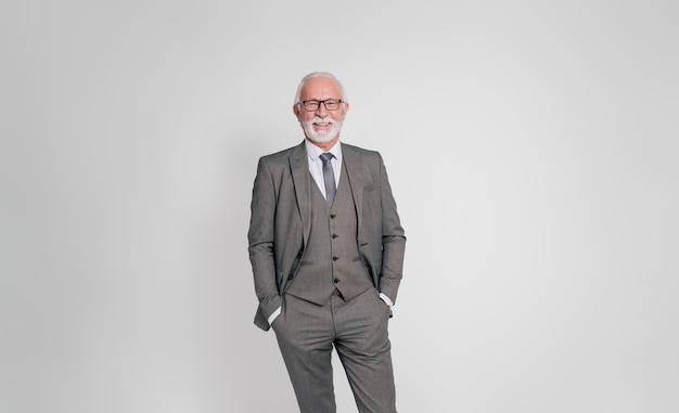 Photo portrait of elderly male professional with hands in pockets standing confidently on white background