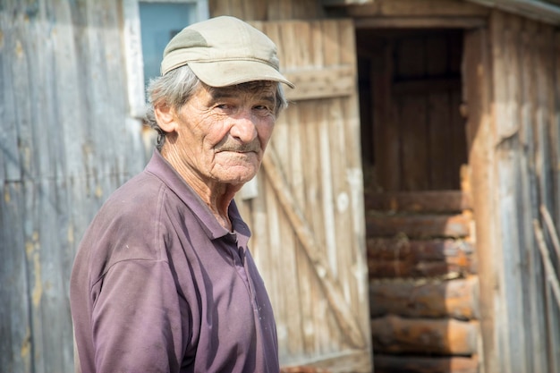 a portrait of an elderly man in a baseball cap and a shirt standing in a rural yard Village life