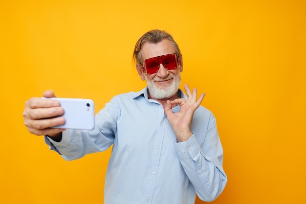 Portrait elderly man in fashionable red glasses with a phone isolated background