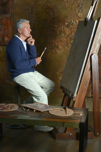 Photo portrait of elderly man painting with easel