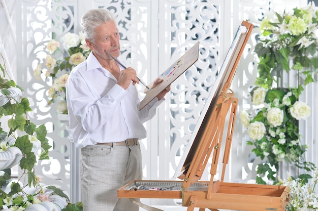 Portrait of elderly man painting with easel
