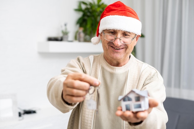 Portrait of elderly man in santa hat hold key small house.