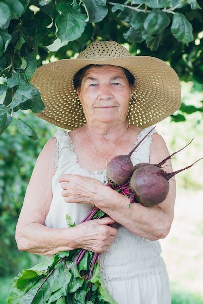 Portrait of an elderly woman in a hat holding a beets