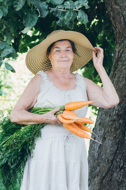 Portrait of an elderly woman in a hat holding a carrot