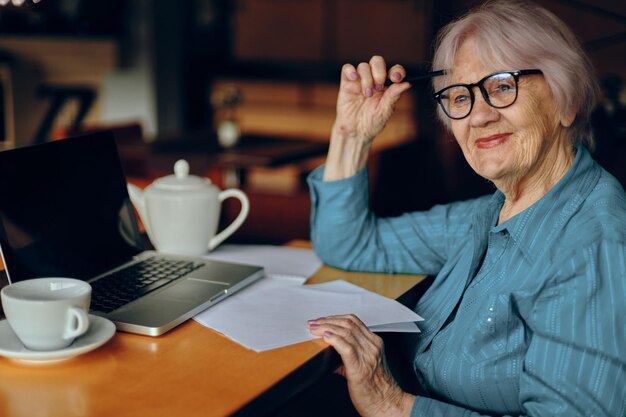 Portrait of an elderly woman with glasses sits at a table in front of a laptop Freelancer works unaltered