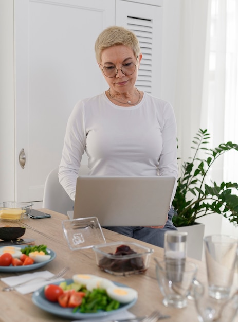 Portrait of an elderly woman with laptop on kitchen looking for tutorial online cooking watching