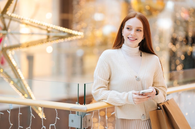 Portrait of elegance smiling young woman holding mobile phone and shopping bags with purchase