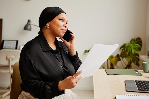 Portrait of elegant black businesswoman calling by smartphone at workplace in minimal office interio