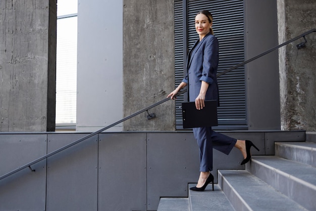 Portrait of elegant business woman in a suit walking down the\
stairs