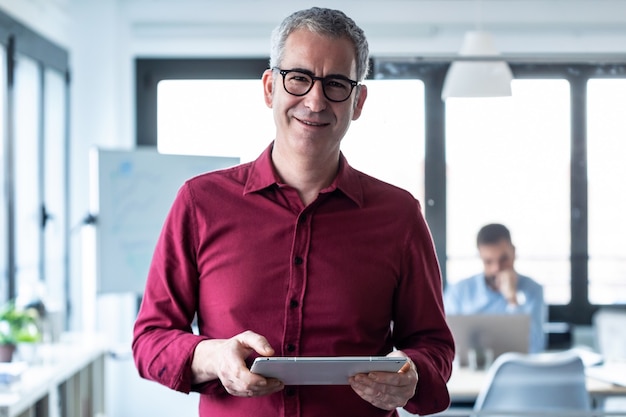 Portrait of elegant businessman looking at camera while working with digital tablet in the office.