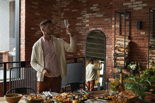 Portrait of elegant mature man inspecting glasses while serving dinner table for Thanksgiving party at home, 