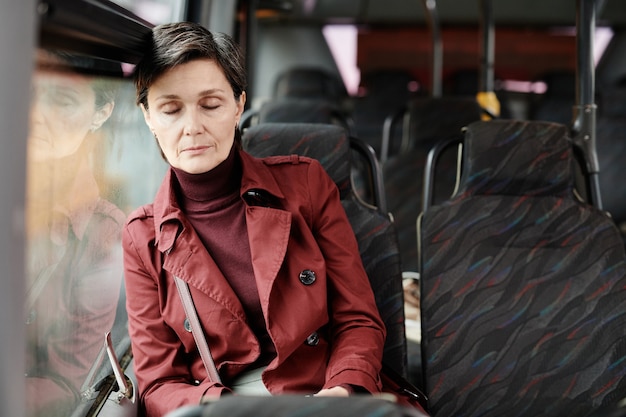 Портрет элегантной зрелой женщины, спящей в автобусе во время поездки на общественном транспорте по городу, копией пространства