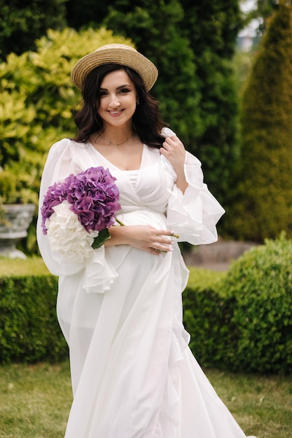 Portrait of elegant pregnant woman in beautiful white dress walking outdoors future mom hold wicker