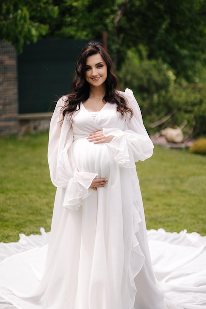 Portrait of elegant pregnant woman in beautiful white dress walking outdoors