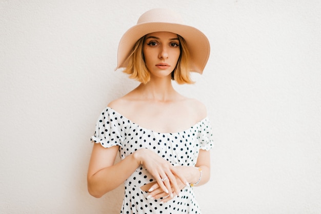 Portrait of elegant stylish blonde short hair girl in hat and dress posing over white
