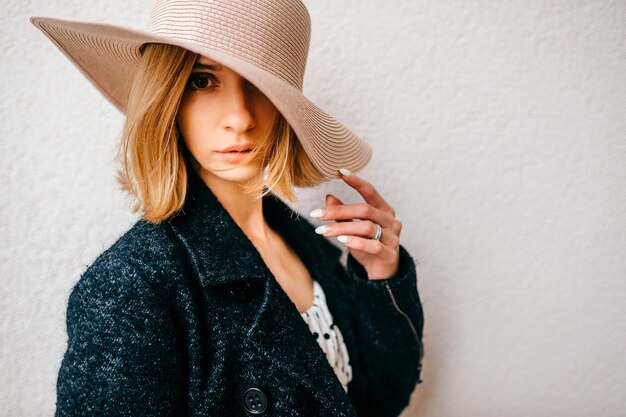 Portrait of elegant stylish blonde short hair girl in hat and jacket posing over white background