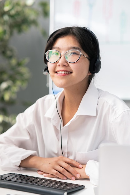 아시아 한국 미인이 있는 안경을 쓴 우아한 여성들은 헤드폰을 끼고 회사 사무실에 앉아 있다